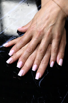Receiving Professional Manicure in Modern Salon. Beautiful, well-groomed women's hands with elegant nails against a dark background. Beauty salon concept: manicures, pedicures. 