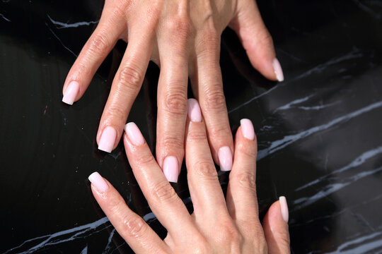 Receiving Professional Manicure in Modern Salon. Beautiful, well-groomed women's hands with elegant nails against a dark background. Beauty salon concept: manicures, pedicures.