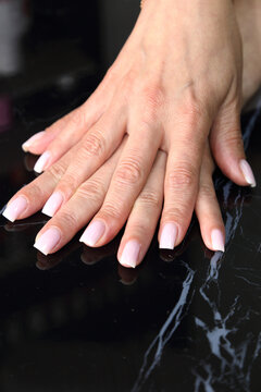 Receiving Professional Manicure in Modern Salon. Beautiful, well-groomed women's hands with elegant nails against a dark background. Beauty salon concept: manicures,