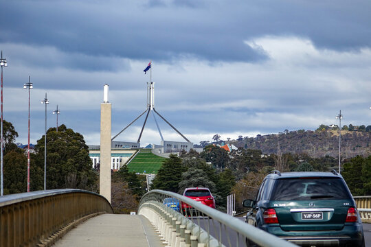 Dramatic View of Australian Parliament House in Canberra, featuring the iconic flagpole and modern architecture under a cloudy sky.