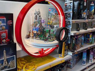 Fototapeta premium Toy store shelf with a displayed building block model under a red circular frame, surrounded by boxed construction sets and a magnifier in the foreground.