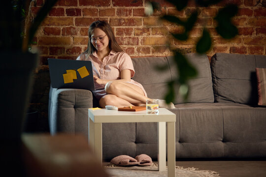 Smiling young woman working remotely from cozy home office with laptop. Concept of flexible work, freelance career, digital productivity and comfortable home workspace.