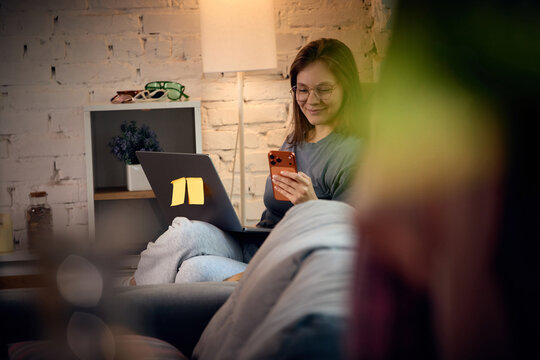 Woman checking smartphone while working with laptop from comfortable home interior. Concept of mobile communication, online services and flexible remote workflow.