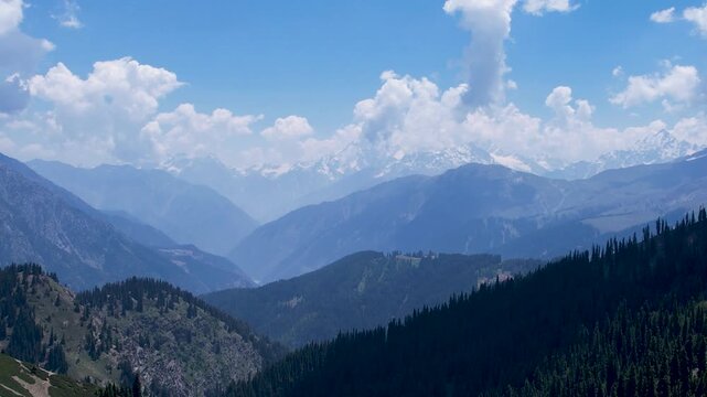 Forested ridges lead toward snow-covered Hindu Kush peaks beneath towering clouds, Kalam, Khyber Pakhtunkhwa, Pakistan