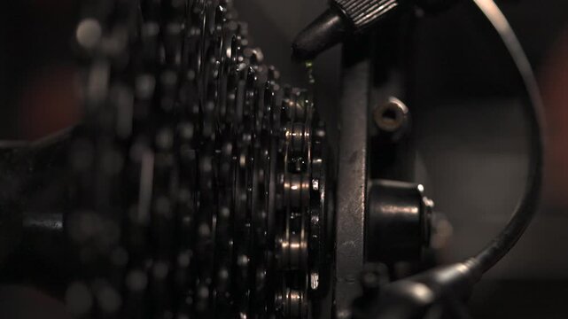 Macro shot of bike chain spinning in mechanic shop as fluid is applied to chain, slo mo, slow motion, tight shot