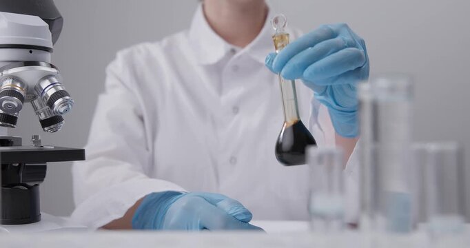 Tracking shot of gloved scientist holding small round flask with oil dark liquid and giving thumbs up on chemical laboratory.