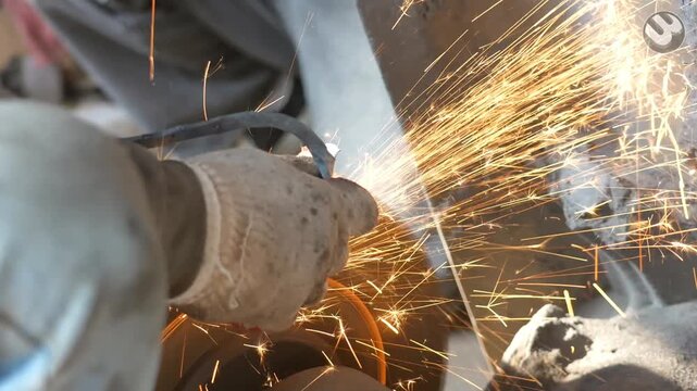 A worker uses a motorized abrasive wheel to grind and sharpen raw steel blades by applying pressure to the metal edge, which generates intense sparks during the industrial maintenance task.
