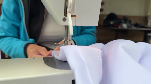 A woman sits on the porch of her house, sewing white fabric sunshades with a sewing machine. The image captures a DIY home improvement project, showcasing craftsmanship, creativity, and preparation fo