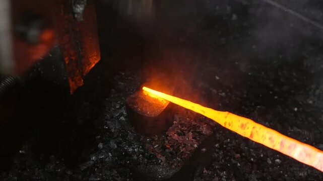 The blacksmith employs a powerful mechanical hammer to shape glowing metal on an anvil, followed by intense reheating within a coal fire furnace for further industrial forging operations.