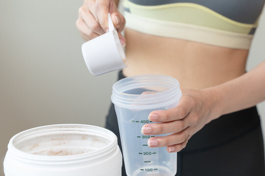 Young sporty woman pouring protein powder into a cup to make replacement food meal after workout