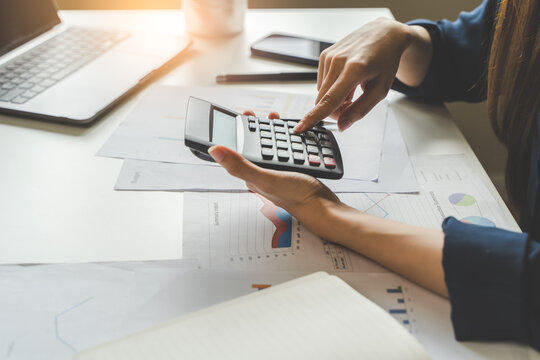 Women business people use calculators to calculate the company budget and income reports on the desk in the office.