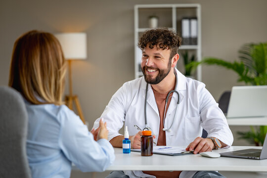 Smiling male doctor consulting with patient at modern medical office discussing treatment and prescriptions