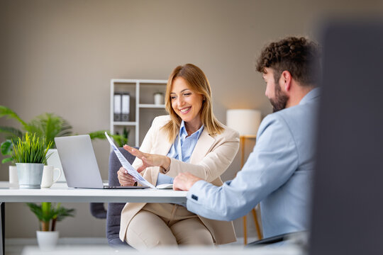 Business meeting with consultant reviewing documents with smiling Caucasian businesswoman and businessman in modern office