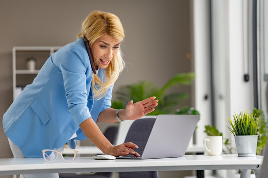 Female business professional video calling on laptop while working at modern office desk