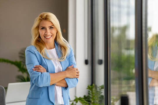 Professional smiling businesswoman standing confidently in modern office with arms crossed
