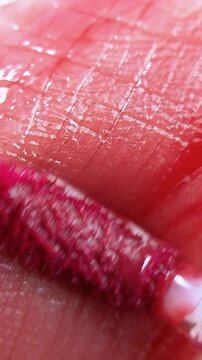 Extreme close up of pink lip tint brush applicator applying color to lip skin surface. Makeup product application, soft pigment texture for beauty concept.