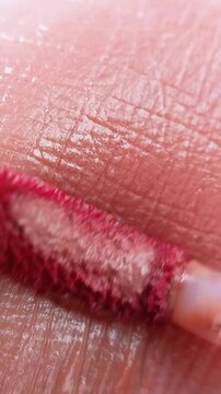 Extreme close up of skin being applied with mocha colored lip tint using a brush. Glossy finish resembling lip texture. Makeup product concept.