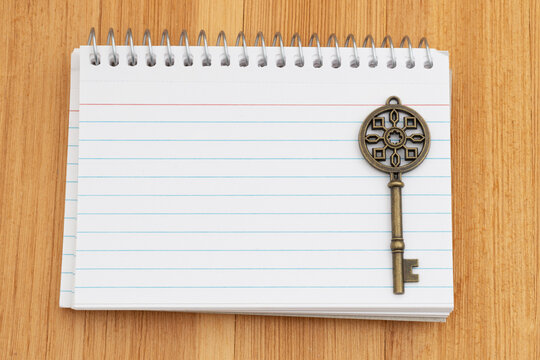 Blank spiral notebook of index cards with old skeleton key on wood desk