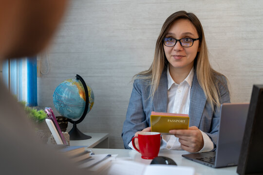 A female tourism manager enthusiastically checks the client's passport at a travel agency or visa application center. Office work, fun conversation and professional communication.