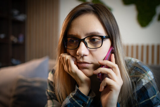 Thoughtful young woman talking on a pink smartphone, resting her chin on her hand. Serious phone call, deep conversation, or receiving bad news.