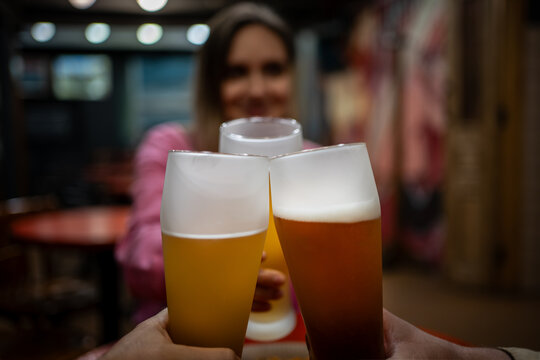 Friends clinking glasses of light beer in a pub. Smiling young woman enjoying a social gathering with refreshing draft beer. Cheers For Us. women Drinking Draft Beer And Clinking Glasses