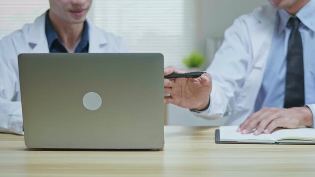 Doctors discussing a medical case together in a modern clinic office, using a tablet and laptop for telehealth, healthcare technology, medical consultation and health insurance planning.