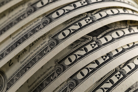 Macro shot of US one dollar bills curved in rows with selective focus on One Dollar text