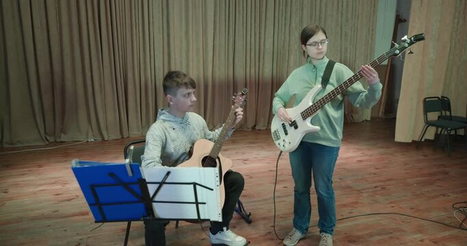 Boy and Girl Practice Playing Music on Stage. Kids Play Guitar and Bass Guitar. 4K 10-bit