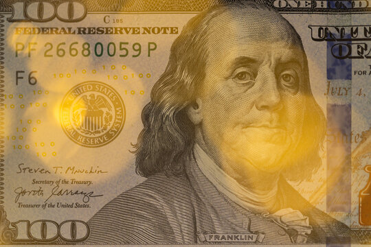 Close-up of US one hundred dollar bill with Benjamin Franklin portrait and warm golden bokeh lights