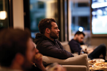 Obraz premium A thoughtful man enjoying a sports event from the comfort of his living room, surrounded by friends, capturing the cozy atmosphere of shared viewing experiences.