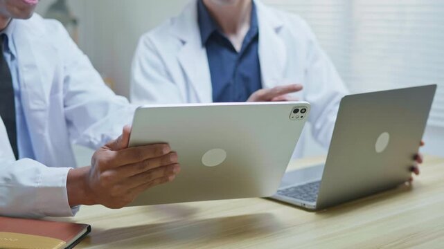 Doctors discussing a medical case together in a modern clinic office, using a tablet and laptop for telehealth, healthcare technology, medical consultation and health insurance planning.