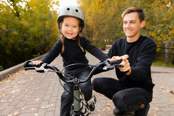 Obraz premium Dad and little girl daughter learning to ride bicycle park having fun together, lifestyle moment