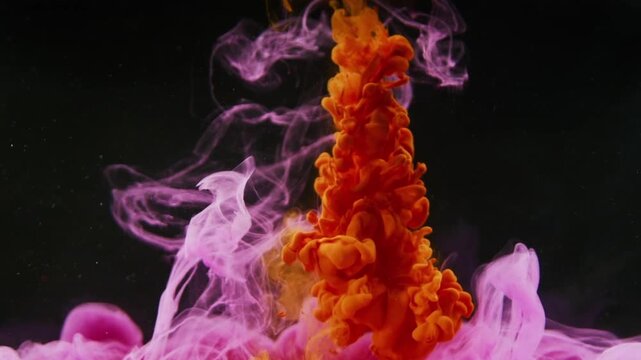 A slow-motion movement of colorful ink in water against a pitch-black background. At the bottom, a soft, cloud-like plume of purplish-pink ink is visible.