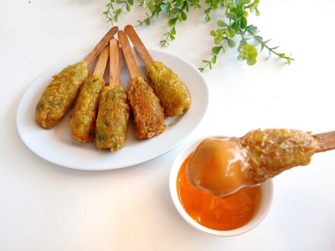 Traditional Indonesian street food called sempol ayam made from minced chicken, tapioca flour, spices, and egg coating. Fried chicken skewers served on a white plate with sweet chili dipping sauce
