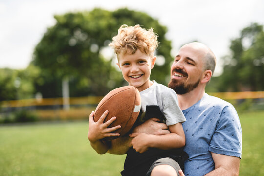 man and young boy playing american football on a court, teaching little player and spending time outdoors