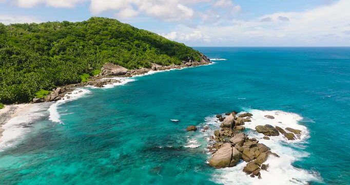 Rocky coastline surrounded by green hills and the blue ocean stretching to the horizon. Seychelles, Mahe. Anse Petit Boileau.