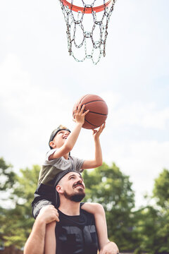 man and young boy playing basketball on a court, teaching little player and spending time outdoors