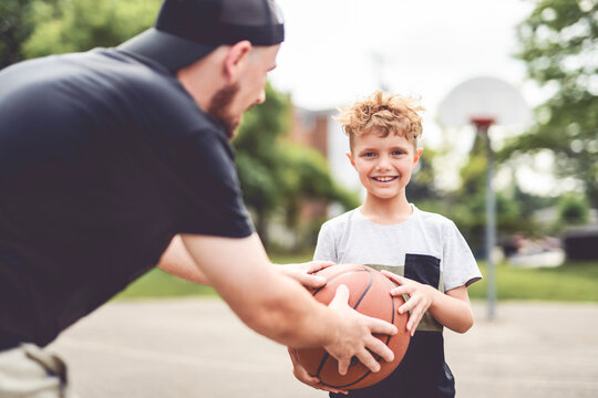 man and young boy playing basketball on a court, teaching little player and spending time outdoors