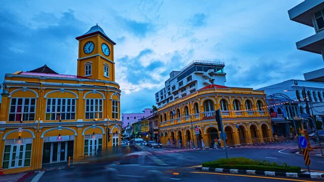 Time lapse Twilight cityscape of Phuket Old Town with its iconic clock tower surrounded by colorful colonial buildings and vibrant urban life in southern Thailand.