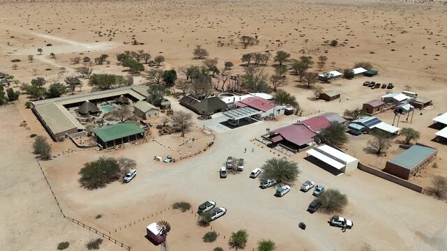 Cinematic aerial footage of a remote tourist lodge and safari camp nestled in the arid desert savanna landscape of Namibia, Africa.