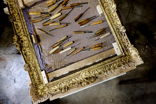 Traditional wood carving chisels on ornate antique frame in artisan workshop
