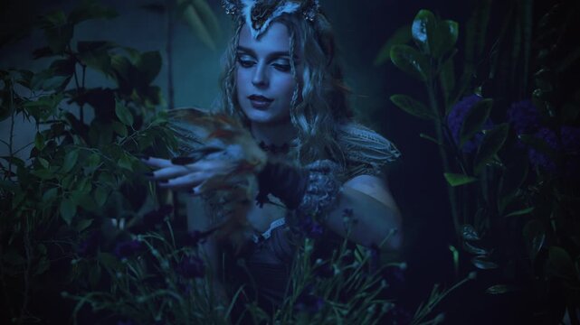 close-up hand with sharp claws black nails evil gothic fantasy woman owl touching flowers green grass plant dark night forest, halloween bird costume. sexy face eyes lips fairy tale elf mystery girl