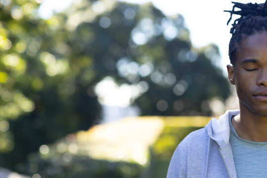 African American man standing eyes closed in sunlit park wearing hoodie and ear stud, copy space