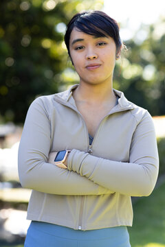 African American woman standing in park wearing beige zip jacket and leggings, showing smartwatch