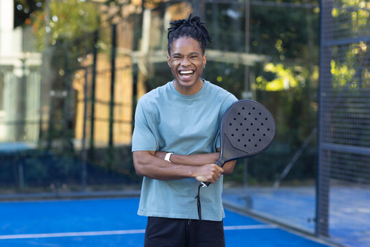 Adult man standing on blue court holding round paddle, wearing light blue tee and black shorts