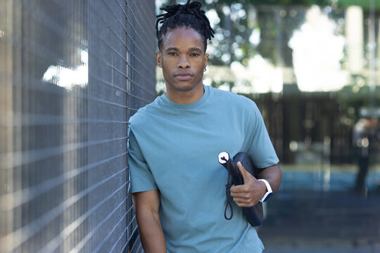 African American man leaning on chainlink fence wearing teal-tee, holding board white-watch at park