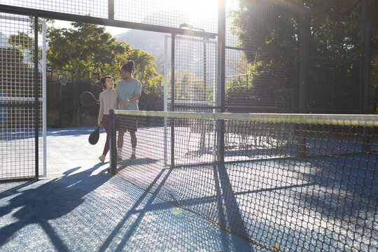 African American couple walking near net on blue padel court carrying solid rackets, copy space
