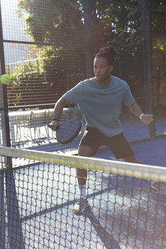 African man preparing to return green ball at net on blue court holding paddle, wearing shirt