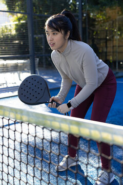 African American woman holding paddle with smartwatch standing in gymwear by net on blue turf court