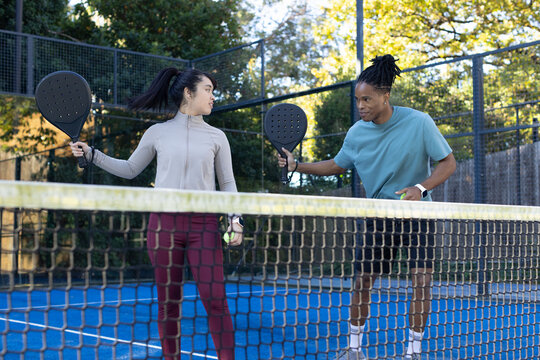 Diverse players in sportswear standing on blue court near net holding dark paddles and green balls